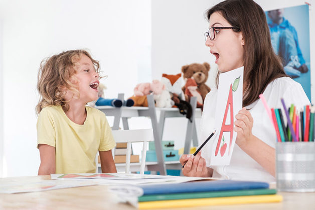 A happy child pronouncing a letter with a speech therapy specialist